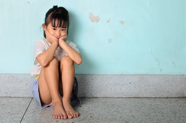 Ledsen och deprimerad liten flicka sitter nära väggen — Stockfoto