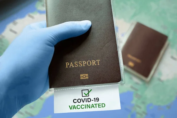 Hand in medical gloves holding passport with COVID-19 Vaccinated note with check mark on map. Coronavirus outbreak situation, traveling after pandemic. Immunity passport risk-free certificate concept.