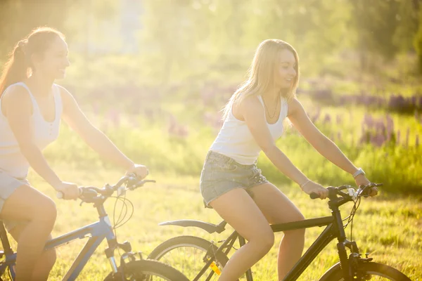 Giovani amiche in bicicletta alla luce del sole — Foto Stock