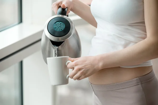 Pregnant woman pouring water from electric kettle — Stock Photo, Image