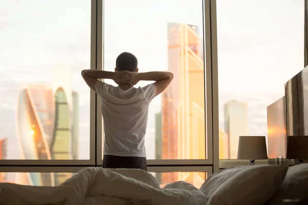 Young man watching sunrise in his bedroom