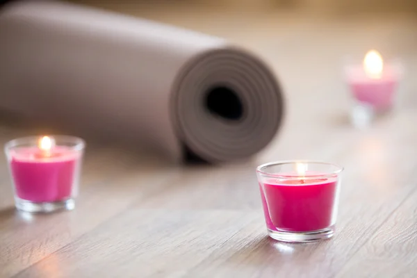 Lighted pink candle and rolled brown yoga, pilates mat on the fl — Stock Photo, Image