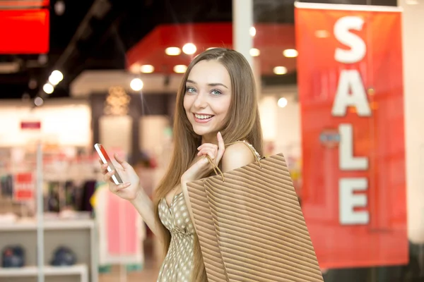 Mujer joven en un centro comercial sosteniendo un teléfono sonriendo — Foto de Stock
