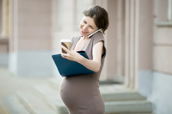 Happy pregnant business woman talking on phone and writing notes — Stock Photo, Image