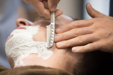 Young man getting a shave with straight razor 