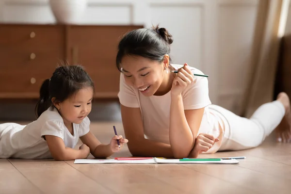 Glückliche junge asiatische Mutter und kleine Tochter zeichnen Bleistifte zusammen — Stockfoto