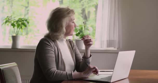 Старша жінка використовує ноутбук відчуває, що втомився знімає окуляри, відпочиваючи — стокове відео