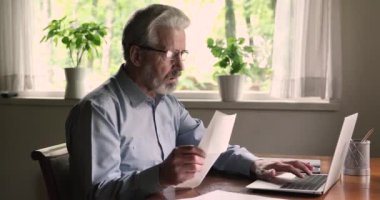 Dizüstü bilgisayar kullanan yaşlı bir adam finansman sağlıyor faturaları ödüyor e-bankacılık kullanıyor