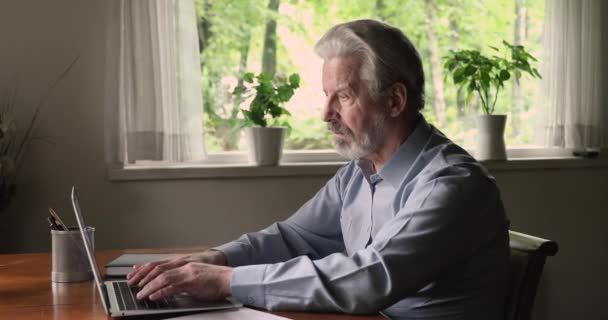 У віці чоловік дивиться на ноутбук, збуджений читанням чудових новин — стокове відео