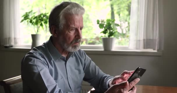 Viejo sosteniendo teléfono inteligente experimenta dificultades con el uso de gadget moderno — Vídeo de stock