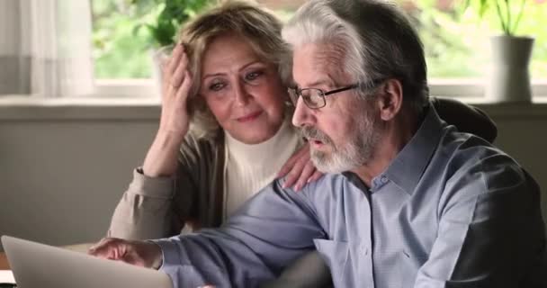 Atractiva pareja de ancianos utilizando el ordenador portátil discutir la compra en Internet — Vídeo de stock