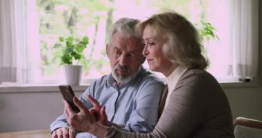 Olgun çift ellerinde akıllı telefon saat fotoğrafları tutuyor, haberleri tartışıyor, internette geziniyor.