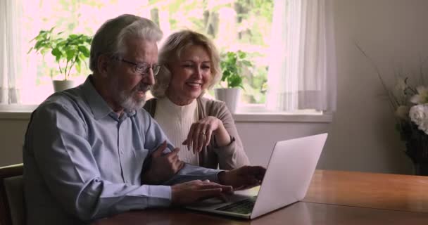 Gelukkig getrouwd ouder paar met behulp van laptop zitten aan tafel indoor — Stockvideo