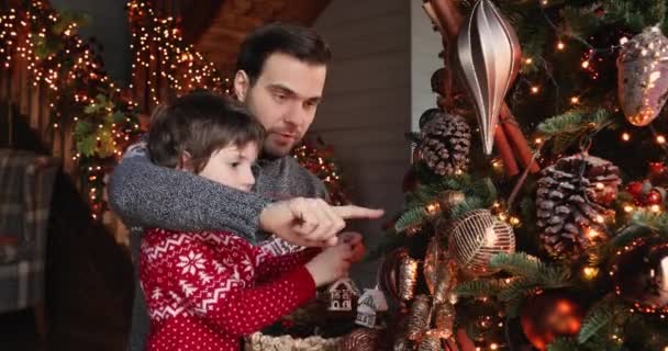 Pequeno filho feliz seu amoroso jovem pai decorar árvore de Natal — Vídeo de Stock