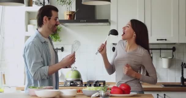 Jonge echtgenoten die keukengerei als microfoon gebruiken, liedjes zingen. — Stockvideo