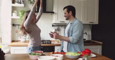 Mutlu genç evli çift mutfakta enerjik bir müzikle dans ediyor..