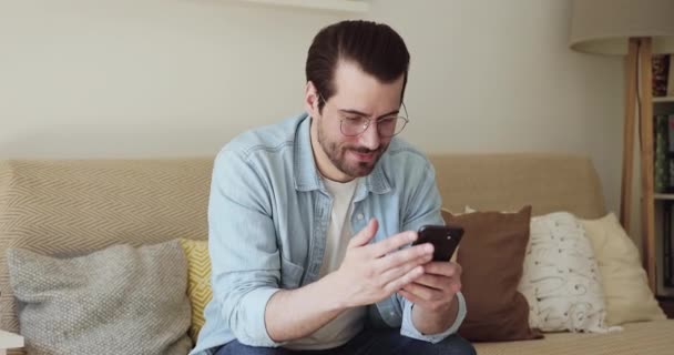 Ontspannen jonge man met behulp van smartphone-toepassingen thuis. — Stockvideo