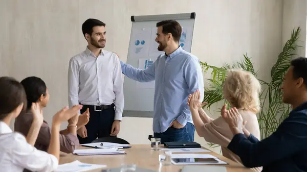 Biznesmen przedstawia męskiego pracownika na spotkaniu grupy w biurze — Zdjęcie stockowe