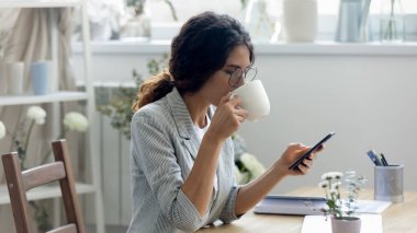 Genç bir kadın sabah kahvesinin tadını çıkarıyor. Akıllı telefonuna bakıyor.