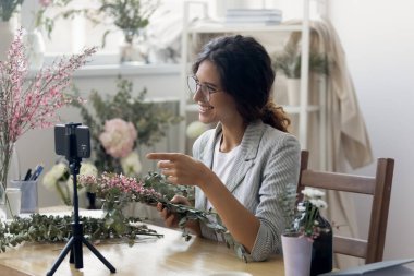 Gülümseyen kadın çiçekçi cep telefonuyla video dersi veriyor.