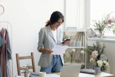 Gülümseyen moda tasarımcısı cep telefonuyla müşteri arıyor.