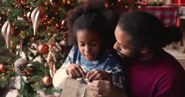 Afrikalı kız elinde bir kutu ile Noel hediyesini açıyor ve babasıyla konuşuyor.