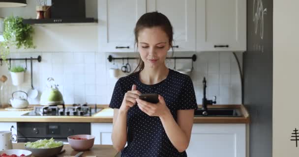 Молодая европейская девушка с помощью мобильного приложения на кухне. — стоковое видео