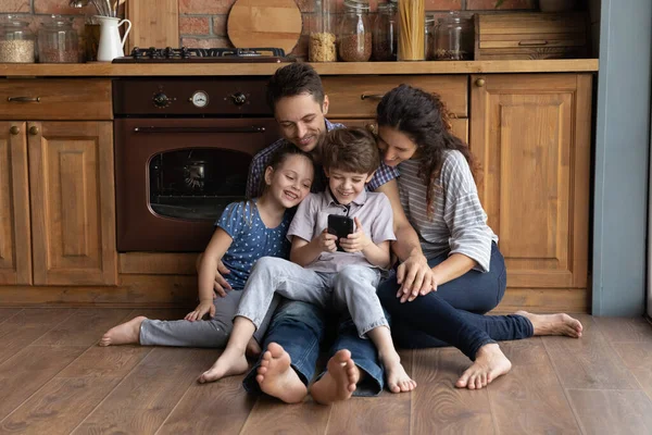 Happy parents with small kids use cellphone in kitchen