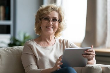 Dijital tablet kullanan güzel, gülümseyen yaşlı kadın portresi.