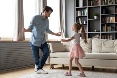 Mutlu genç baba gülümseyen kıza dans hareketlerini gösteriyor..