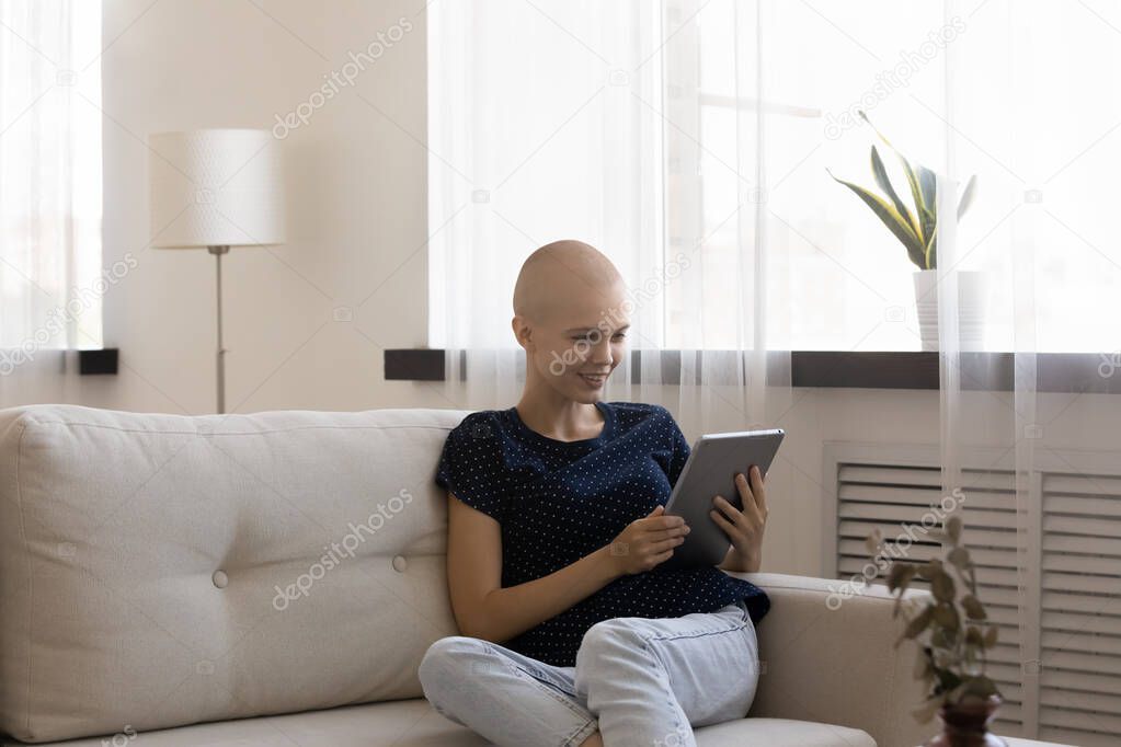 Happy hairless woman holding computer tablet, sitting on couch