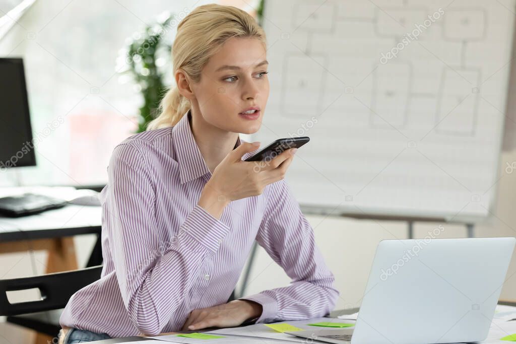 Concentrated young female employee is sending voicemail.
