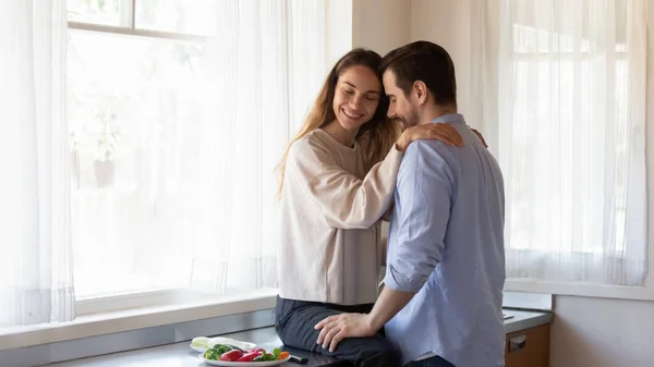 Giovane donna seduta su cucina controsoffitto abbracciando spalle maschili — Foto Stock