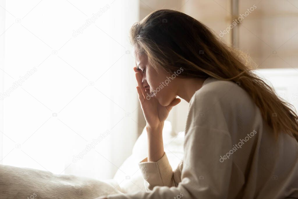 Depressed young woman sitting at home alone crying in silence