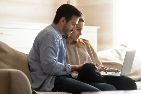 Geconcentreerde man en vrouw zitten op comfortabele bank met behulp van de computer — Stockfoto