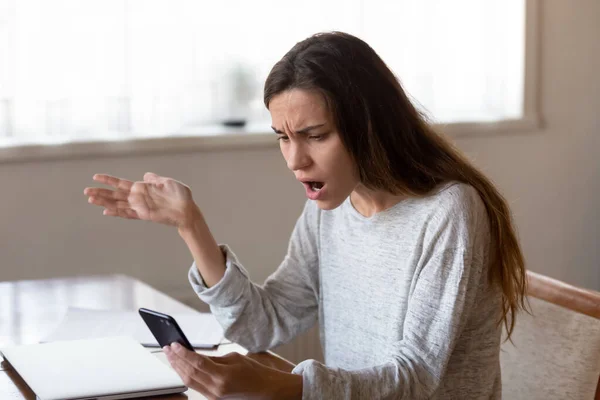 Mujer joven enojada mirando en la pantalla del teléfono móvil que tiene problemas — Foto de Stock