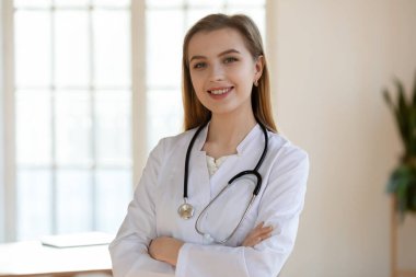 Gülümseyen milenyum kadın doktor elleri göğsünde poz veriyor.