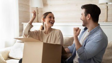 Overjoyed millennial married couple receiving big cardboard package by mail clipart