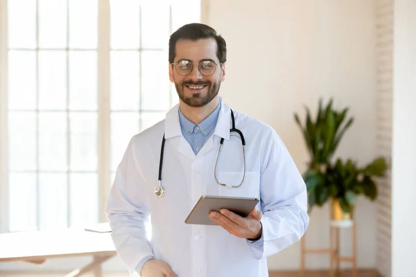Portrait of happy confident young male doctor with tablet pc