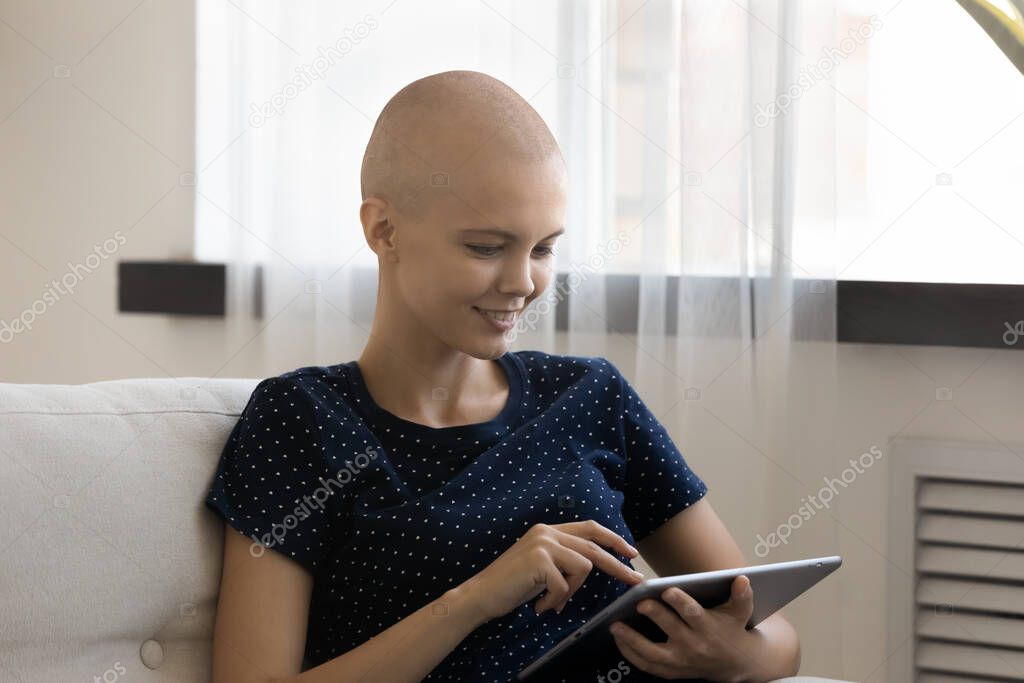 Smiling hairless woman using tablet, chatting, surfing internet at home