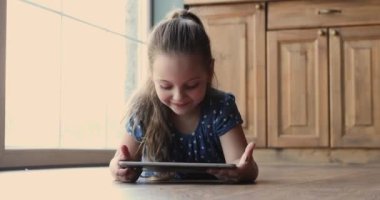 Tablet kullanan çocuk evdeki ahşap sıcak zeminde yatıyor.