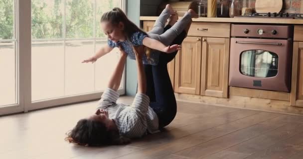 Mamma liggande på golvet lyfter upp dottern på utsträckta armar — Stockvideo