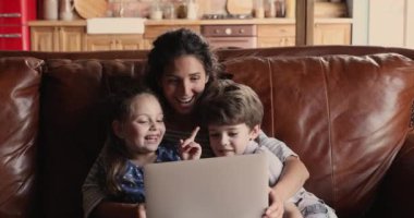 Anne ve çocuklar kanepede oturup dizüstü bilgisayarda çizgi film izliyorlar.
