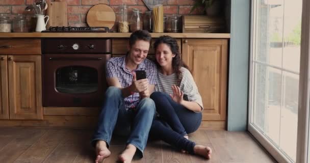 Pareja relajarse en el suelo en la cocina divertirse con el teléfono inteligente — Vídeo de stock