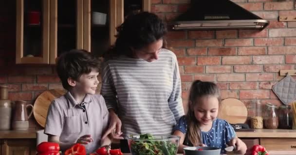 Zorgzame mam en kleine kinderen bereiden samen salade in keuken — Stockvideo