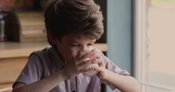 Pequeño niño sentarse en la cocina sosteniendo vidrio beber leche — Vídeos de Stock