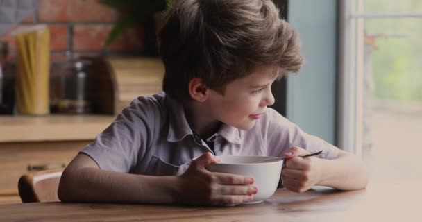 Niño sentado a la mesa comiendo copos de maíz con leche — Vídeos de Stock