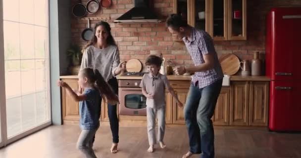 Levendig paar speelse kinderen luisteren funky muziek dansen in de keuken — Stockvideo