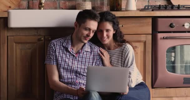 Par sitta på golvet i köket spendera tid med hjälp av laptop — Stockvideo