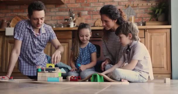 Familia con niños reunidos en la cocina juegan juntos ferrocarril juguete — Vídeo de stock